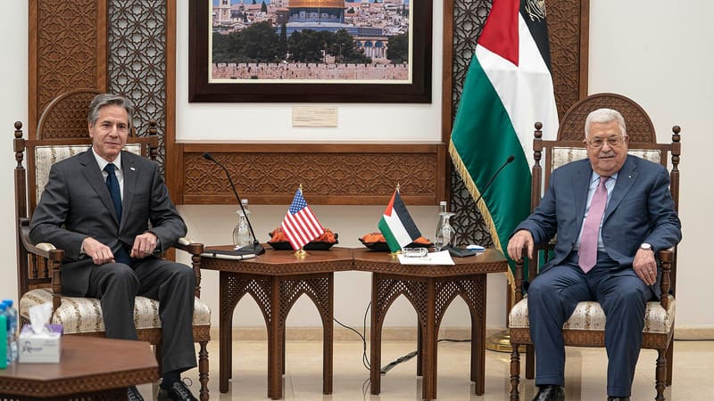 Antony Blinken and Mahmoud Abbas seated in armchairs in Ramallah, with US and Palestinian flags between them