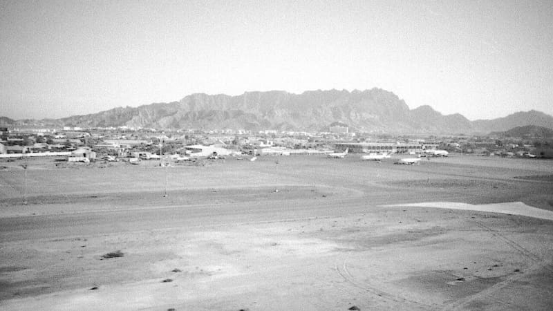Black and white view across Aden airport's airfield with parked airliners and mountains behind