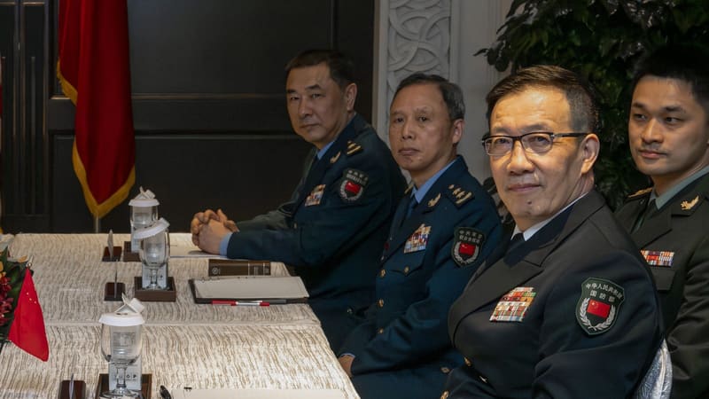 Admiral Dong Jun in naval uniform seated with PLA officers at a conference table, Chinese flag behind