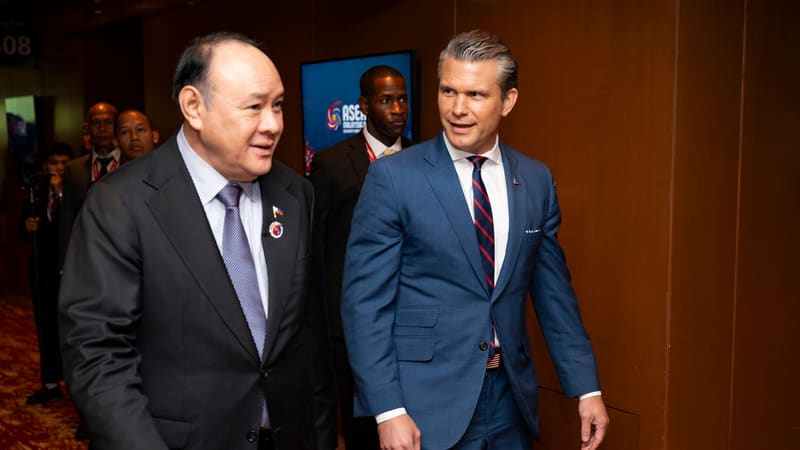 Gilberto Teodoro Jr. and Pete Hegseth walk together down a conference centre corridor
