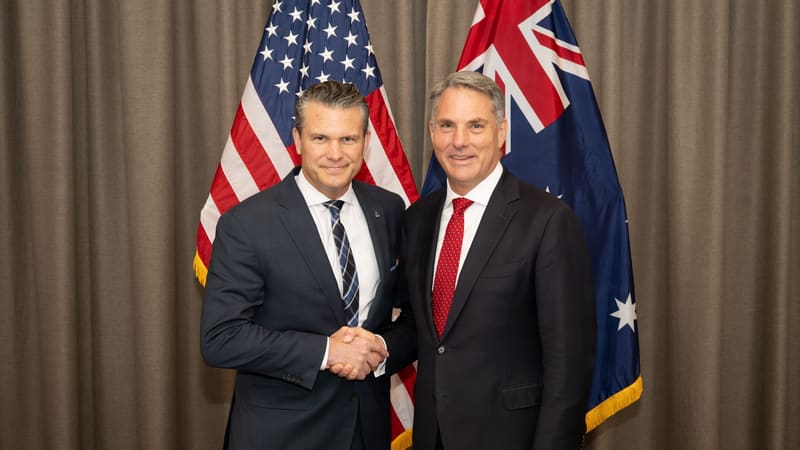 Pete Hegseth shakes hands with Richard Marles in front of U.S. and Australian flags