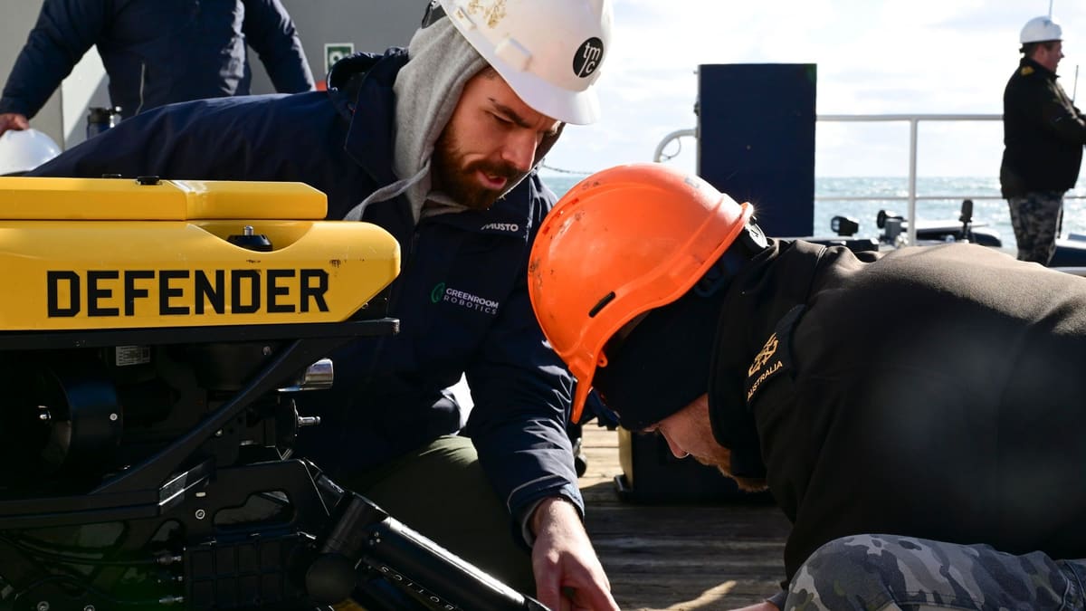 Two men in hard hats adjust a yellow Defender underwater robot on a ship's deck at sea