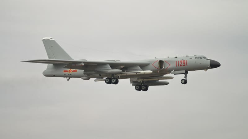Grey Xian H-6K bomber with red serial number 11291 and missiles under its wings landing against an overcast sky.