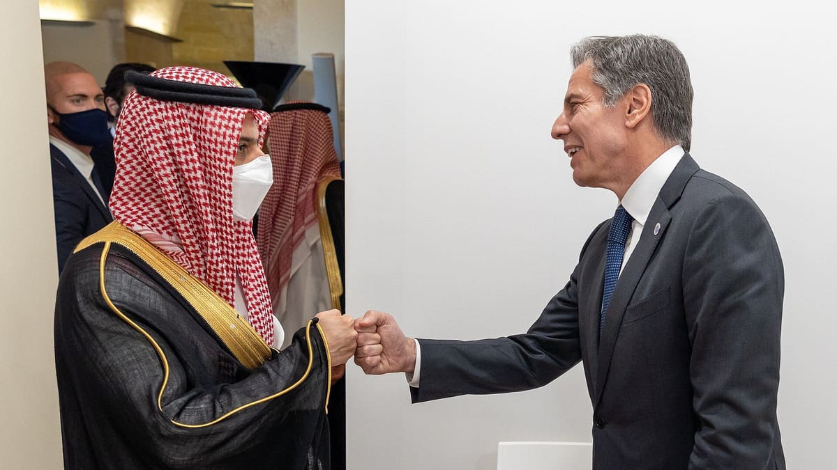 Prince Faisal bin Farhan, in a red-checked headscarf and white face mask, and Antony Blinken exchange a fist bump in 2021.