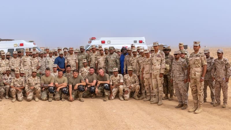 Large group of Egyptian, Saudi and US soldiers in desert uniforms posing in front of ambulances