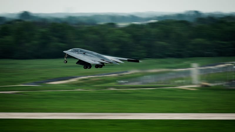A B-2 Spirit lifting off from a green airfield with its landing gear still down