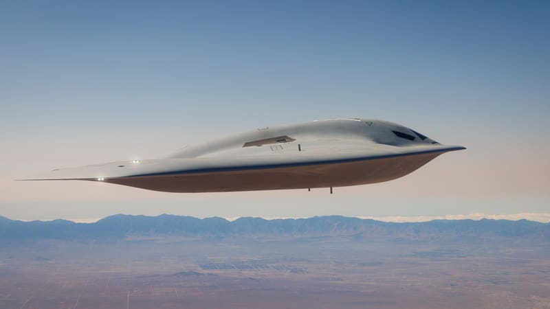 A grey B-21 Raider stealth bomber flying over the California desert, seen from the side and about eye level