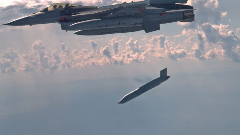 An F-16 fighter above clouds with a long-range cruise missile falling away beneath it after release.