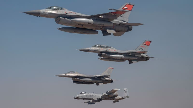 Two Egyptian F-16s with red tail flashes fly above a US F-16 and A-10 against a blue sky