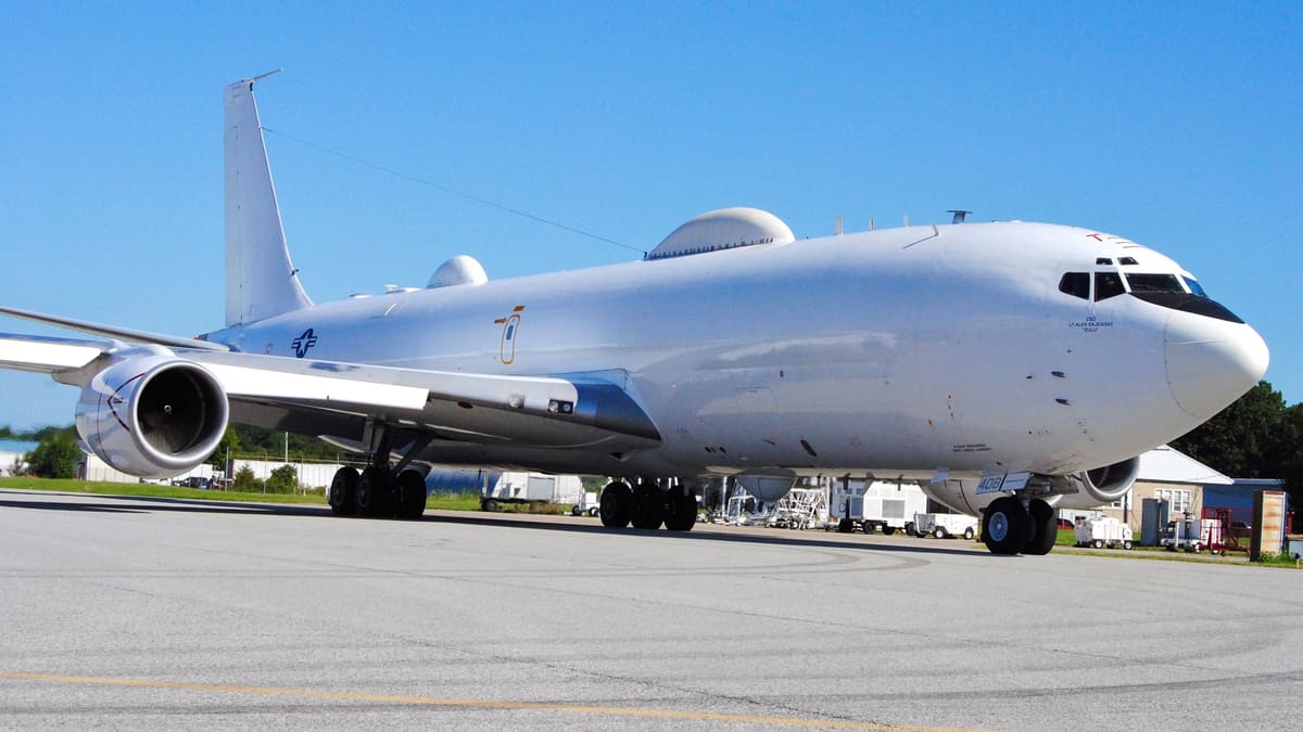 A white E-6B Mercury aircraft parked on a sunny airfield ramp, seen from the front right