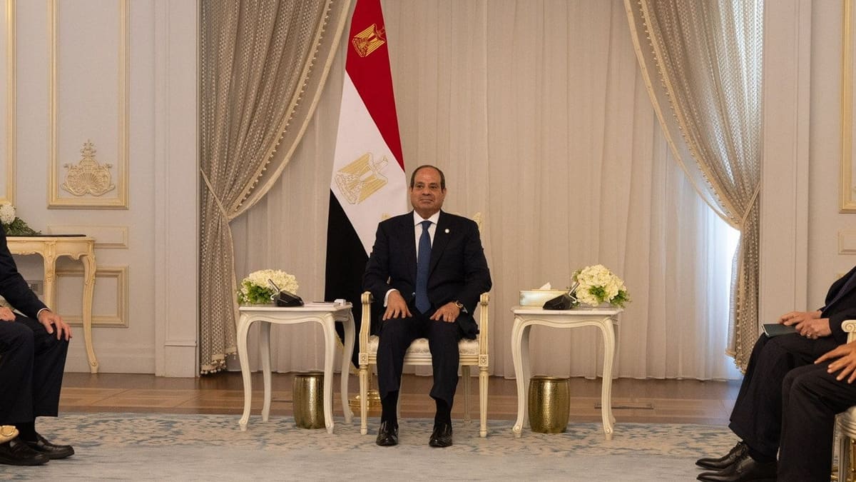 Egyptian President Abdel Fattah el-Sisi seated before an Egyptian flag in a formal reception room, delegations at his sides