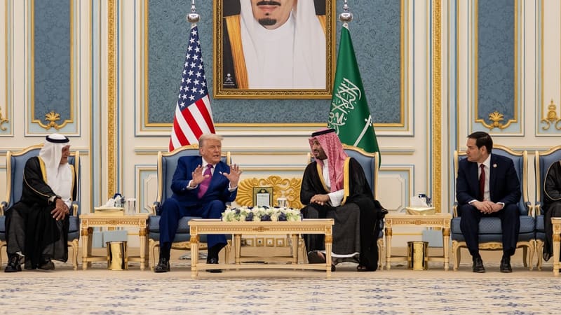 Donald Trump gestures to Mohammed bin Salman as they sit between US and Saudi flags under King Salman's portrait