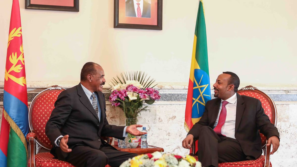 Eritrean President Isaias Afwerki, left, and Ethiopian Prime Minister Abiy Ahmed talk in red armchairs beside their flags