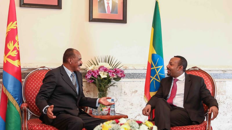 Eritrean President Isaias Afwerki, left, and Ethiopian Prime Minister Abiy Ahmed talk in red armchairs beside their flags