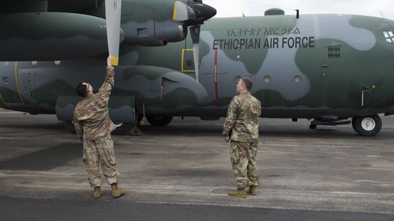 Two U.S. Air Force advisers inspect a green camouflaged Ethiopian Air Force C-130 Hercules on an airbase apron
