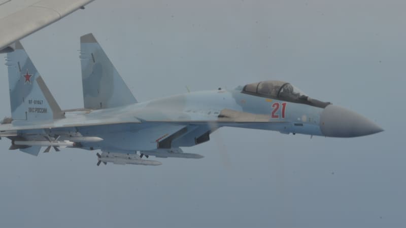 A Russian Su-35S fighter numbered 21, carrying missiles, flies beside the wing of a U.S. Navy patrol aircraft