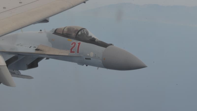 Close view of the nose and cockpit of a grey-blue Russian Su-35S fighter numbered 21 in flight