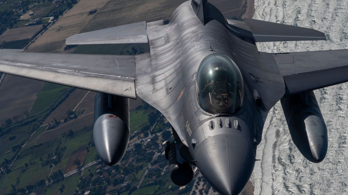 Portuguese Air Force F-16 fighter seen head-on in flight, with two external fuel tanks, over farmland and coastline