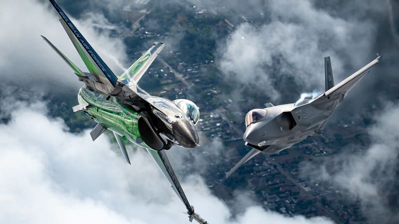 A green-painted Belgian F-16 display jet banks beside a grey U.S. Air Force F-35A above clouds