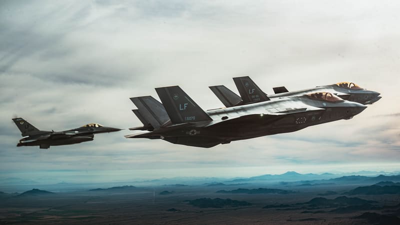 Grey U.S. Air Force F-35A stealth fighters fly in formation with a smaller F-16 over the Arizona desert