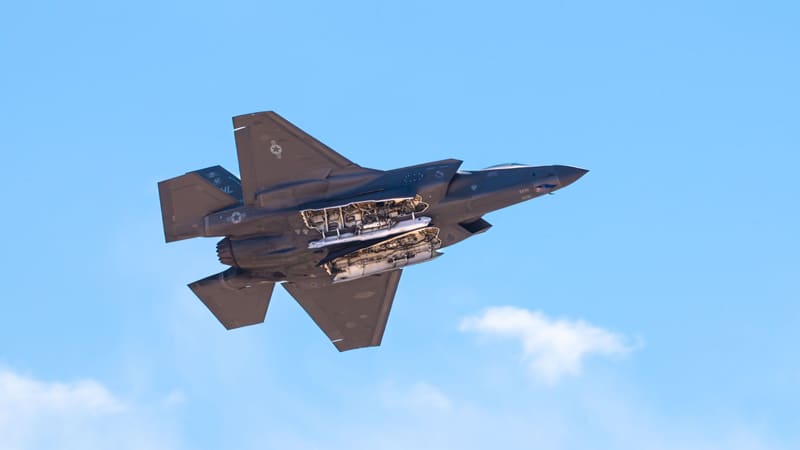 A U.S. Air Force F-35A seen from below banks with both internal weapons bay doors open against a blue sky