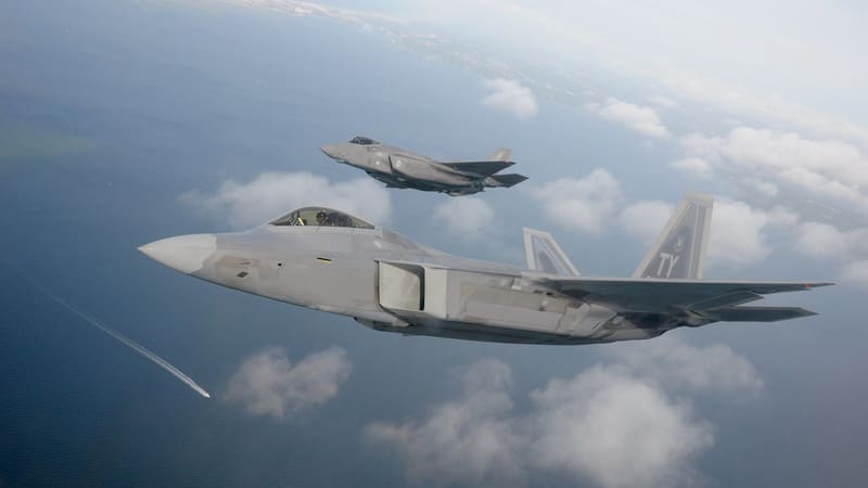 F-22 Raptor with twin tail fins in the foreground and a smaller F-35A Lightning II flying above and behind it