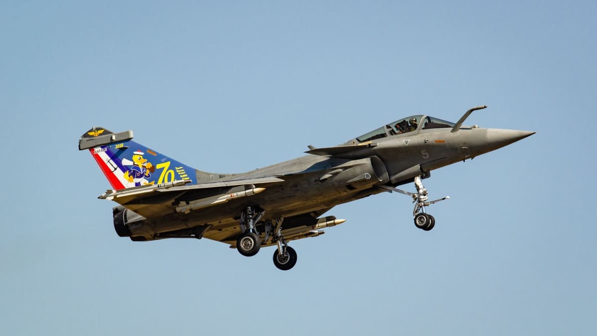 French Navy Rafale M fighter with anchor and cartoon-duck anniversary tail art, landing gear down, blue sky