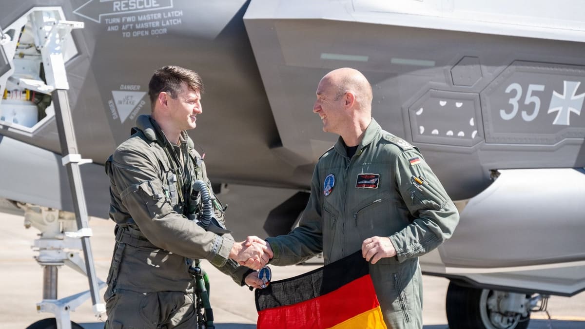 U.S. and German pilots shake hands as the German officer holds a flag beside an F-35A marked with the Iron Cross