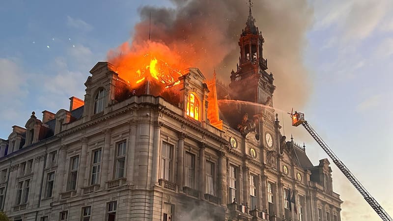 Flames and smoke pour from the roof of Limoges city hall as a firefighter sprays water from an aerial ladder