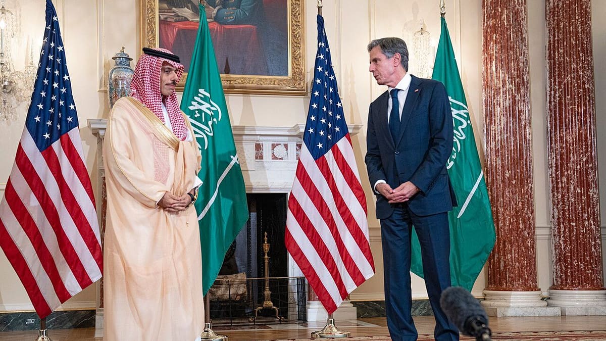 Prince Faisal bin Farhan, left, and Antony Blinken, right, face each other between US and Saudi flags.