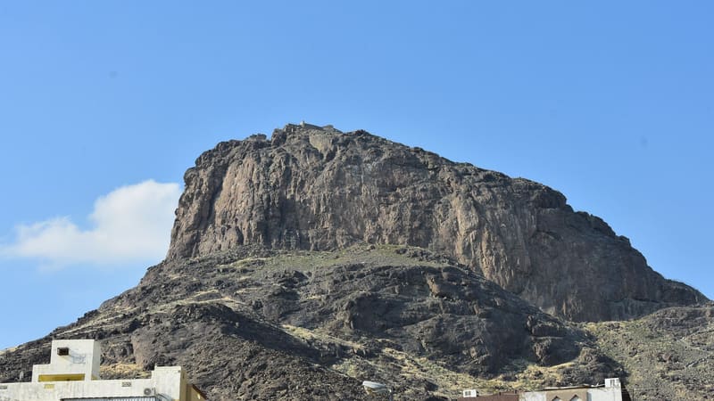 The rocky peak of Jabal al-Nur rising above low buildings on the edge of Mecca under a blue sky.