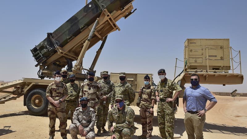 Masked military personnel pose in front of a raised Patriot missile launcher in the desert