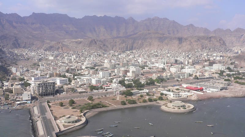 Aerial view of Aden's Crater district, dense low buildings below jagged volcanic mountains and a small bay