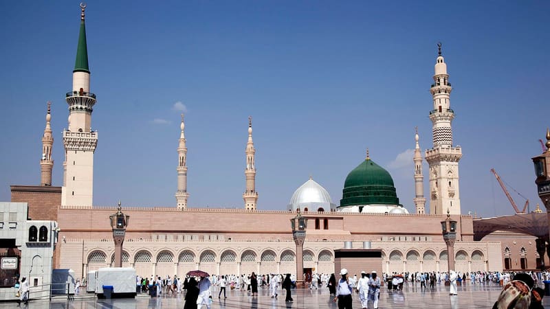 The Prophet's Mosque in Medina with its green dome and minarets, pilgrims walking across the courtyard