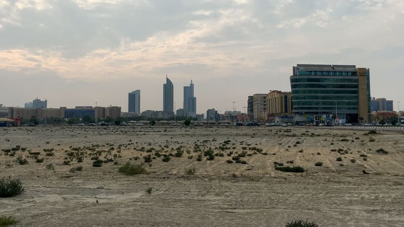 Al Khobar skyline with tall towers beyond an open sandy lot under a cloudy sky