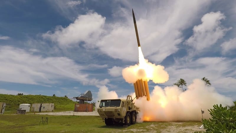 THAAD interceptor rising from a truck-mounted launcher in a cloud of white smoke under a blue sky