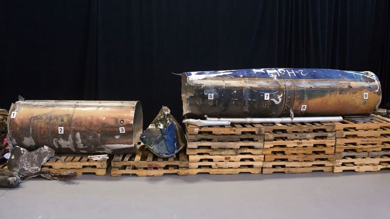 Burnt, numbered sections of ballistic missile wreckage laid out on wooden pallets against a dark curtain