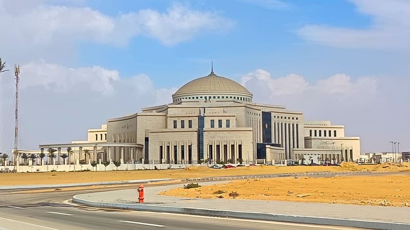 Domed stone House of Representatives building in Egypt's New Administrative Capital across a sandy lot under a blue sky