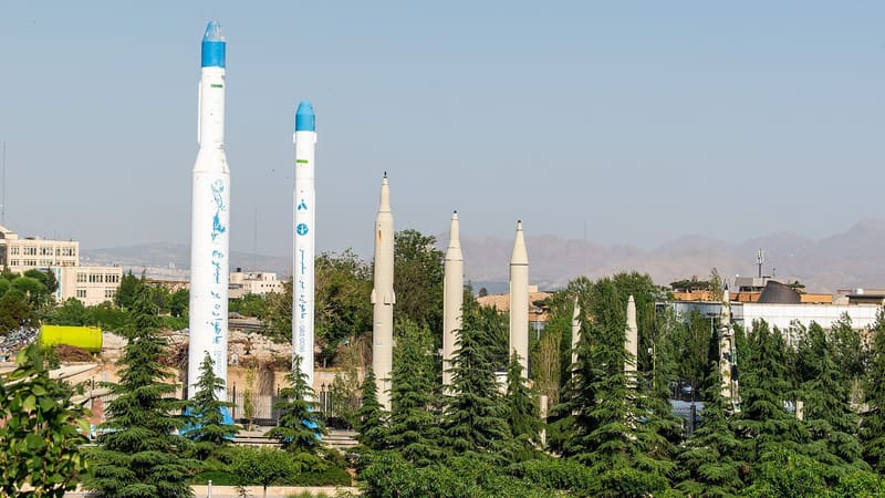 Iranian ballistic missiles and two white-and-blue space launchers on display among trees at a Tehran museum