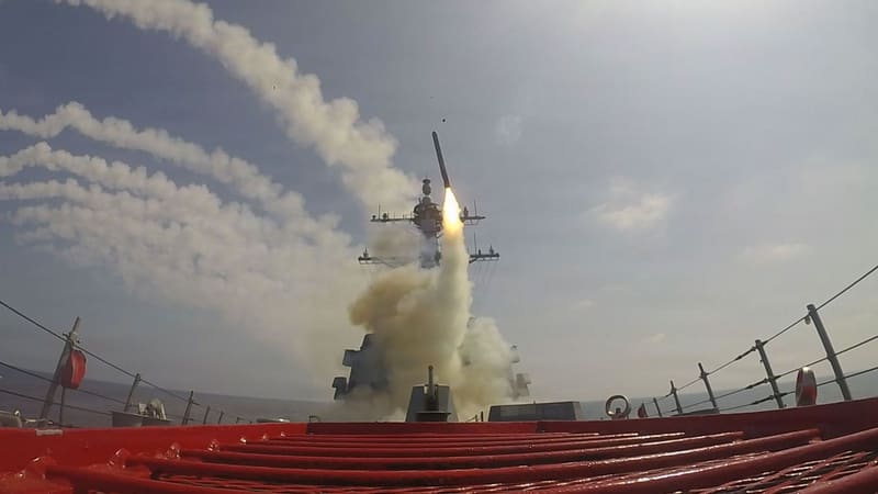 USS Frank E. Petersen Jr. fires a Tomahawk cruise missile as smoke trails from other launches cross the sky