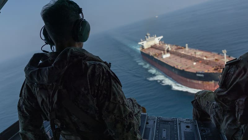 Officer on a helicopter ramp watching a large tanker sail through the strait below