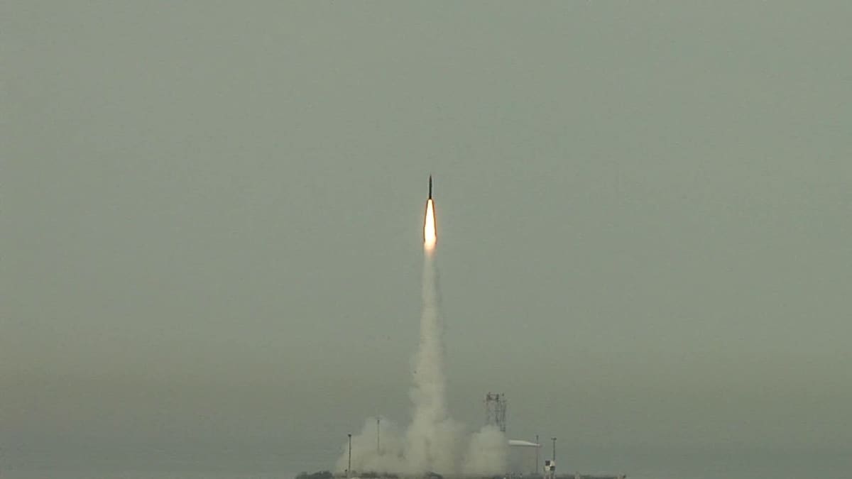 An Arrow 3 interceptor climbs on a bright exhaust plume above a coastal launch site under grey sky