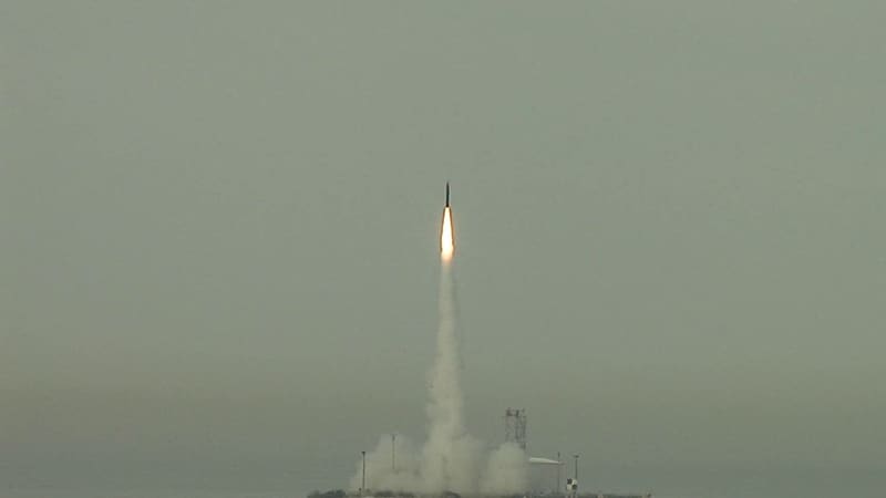 An Arrow 3 interceptor climbs on a bright exhaust plume above a coastal launch site under grey sky