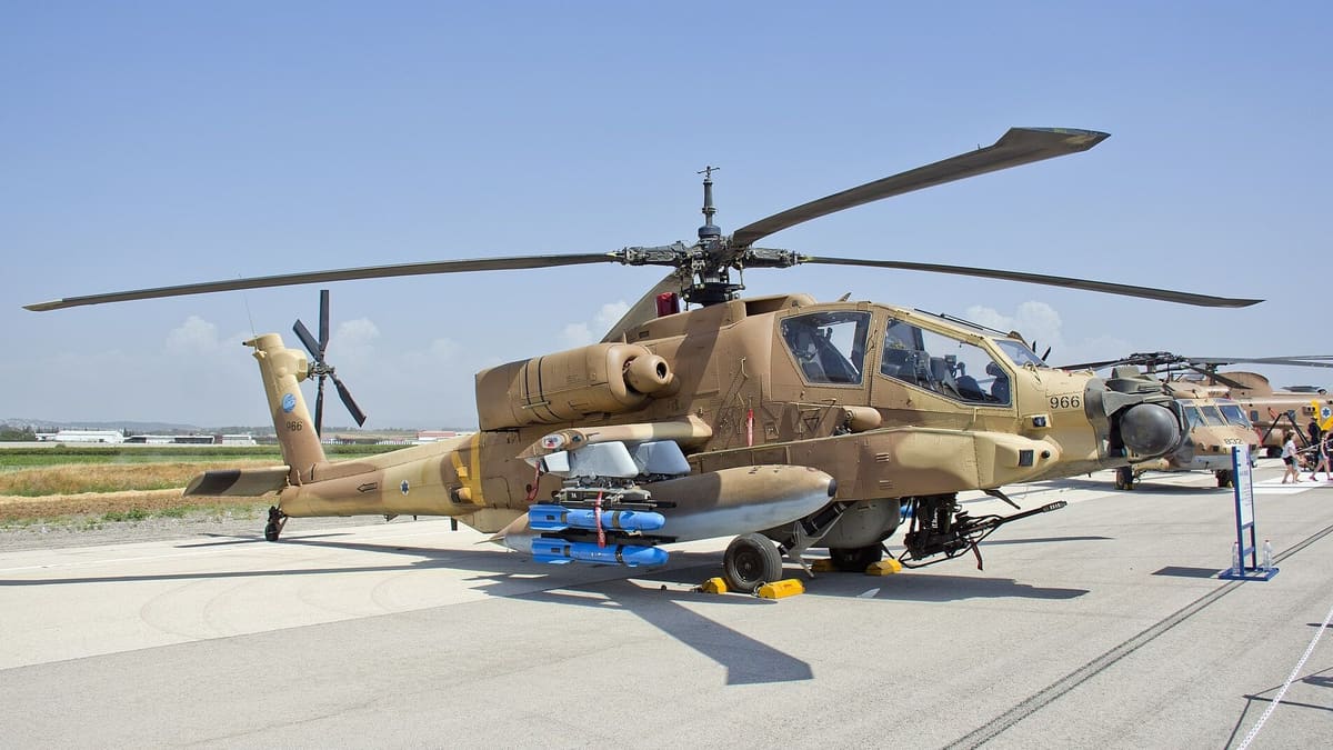 An Israeli Air Force AH-64A Apache in sand camouflage parked on an apron with Hellfire training rounds on its rails