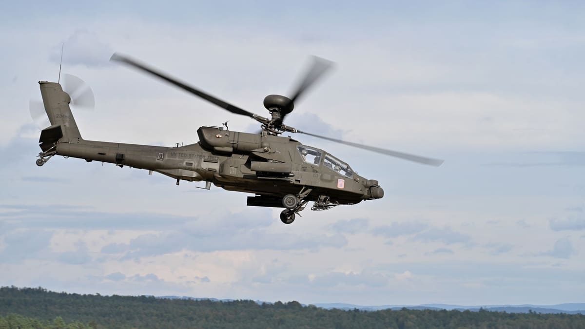 A U.S. Army AH-64E Apache Guardian attack helicopter banking in flight above a forested training area