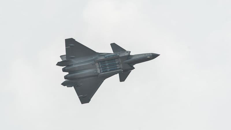 Underside of a Chinese J-20 stealth fighter in flight with its main weapons bay doors open and missiles inside