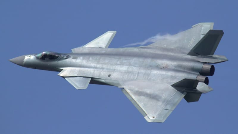 A Chinese J-20 stealth fighter banks in flight against a clear blue sky, showing its canards and twin engines