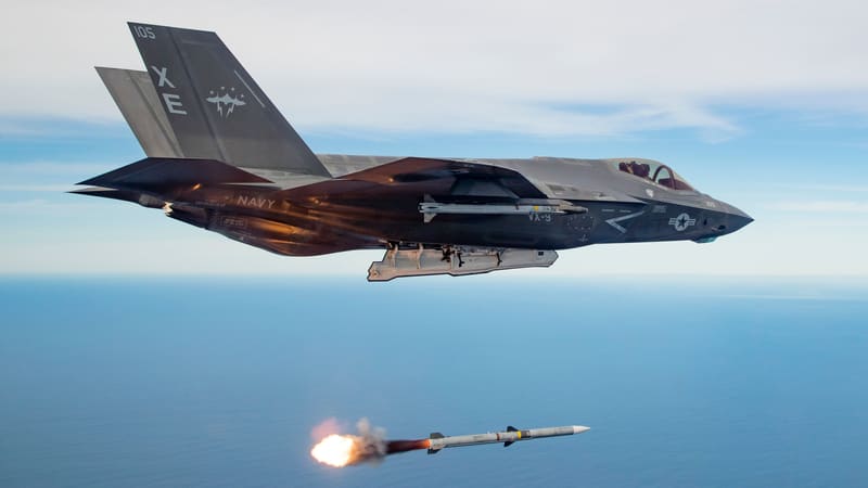 A U.S. Navy F-35C stealth fighter flies over the sea as an AIM-120 missile it launched speeds away below
