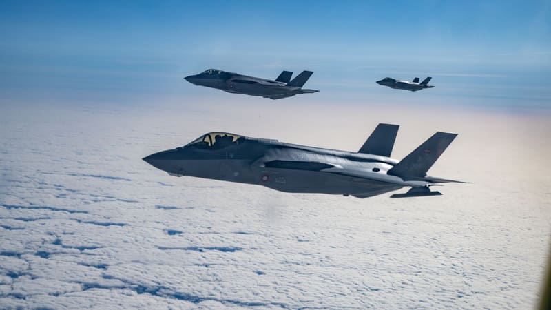 Three grey Royal Danish Air Force F-35A stealth fighters flying in formation above a layer of white cloud.