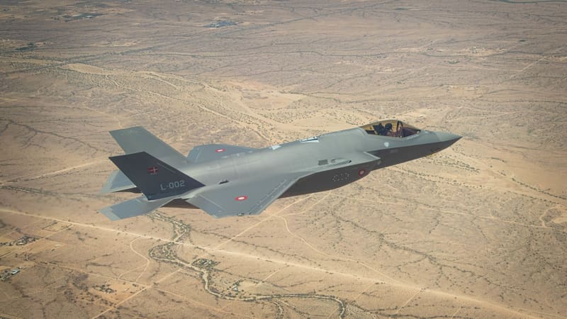 A Royal Danish Air Force F-35A with tail number L-002 flying over brown Arizona desert.